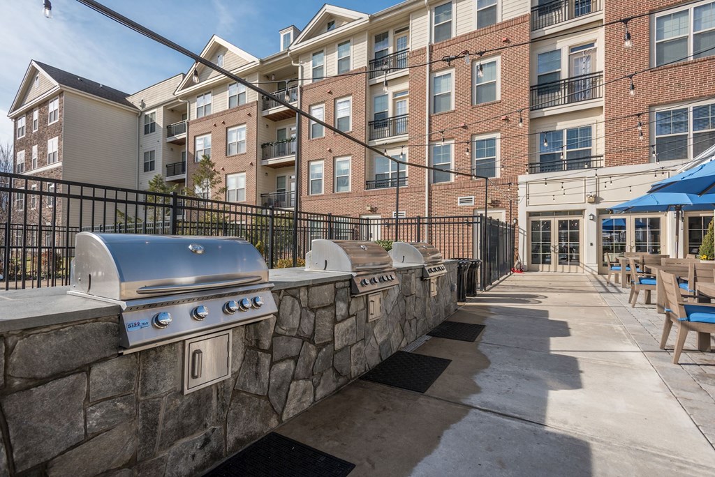 an outdoor patio with a grill and picnic tables and an apartment building