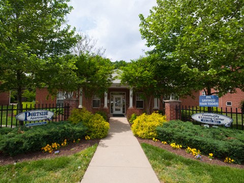 the front of a brick building with a sidewalk and a garden