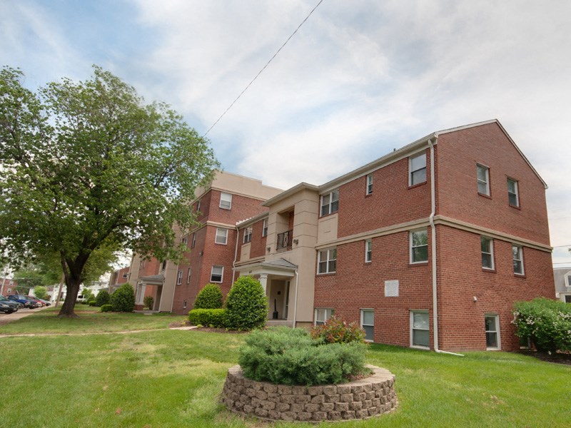 a large brick apartment building with a green lawn and a tree