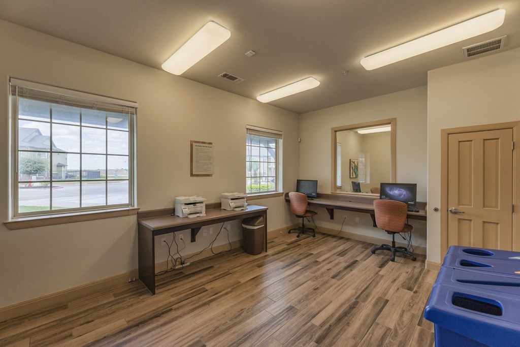 a room with a computer desk and chairs and a window