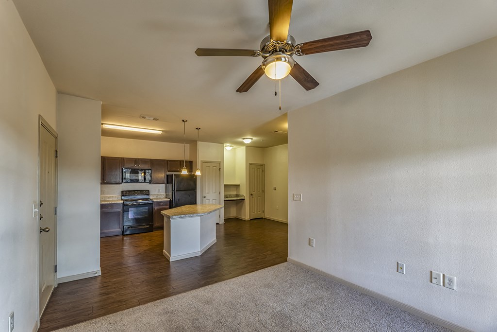 an empty living room with a ceiling fan and a kitchen