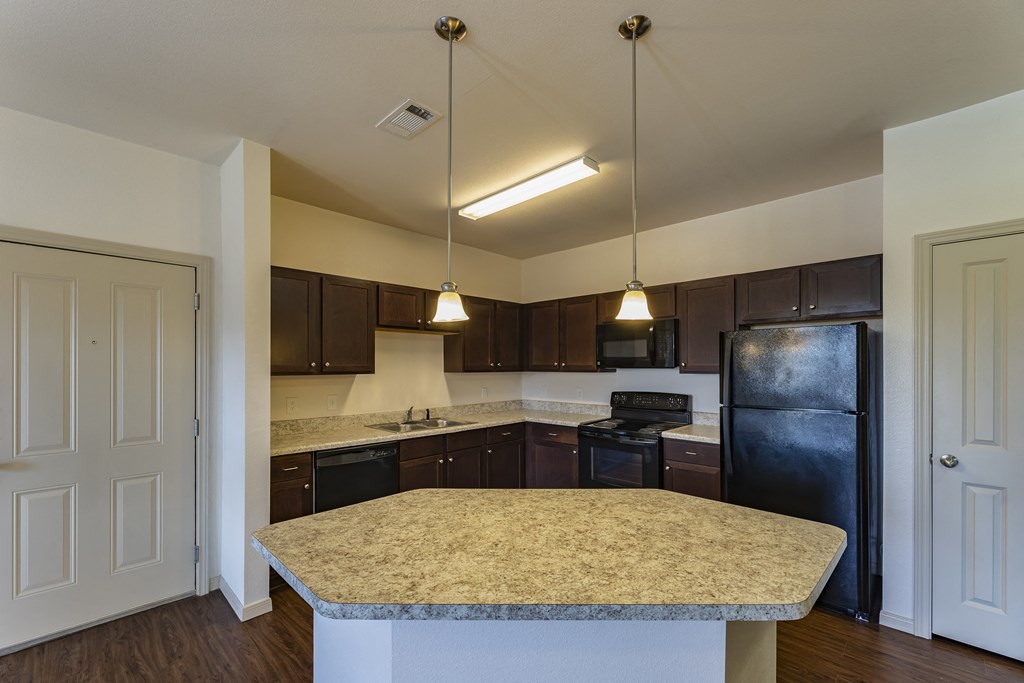 an empty kitchen with a granite counter top and a black refrigerator