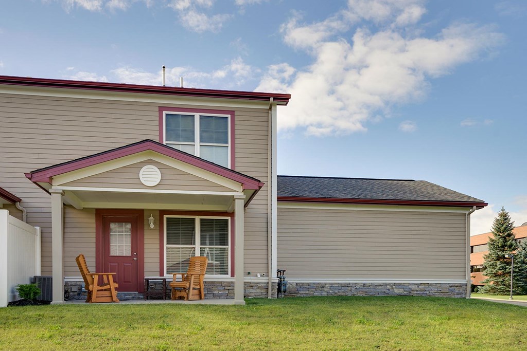 the front of a tan house with a red door and rocking chairs