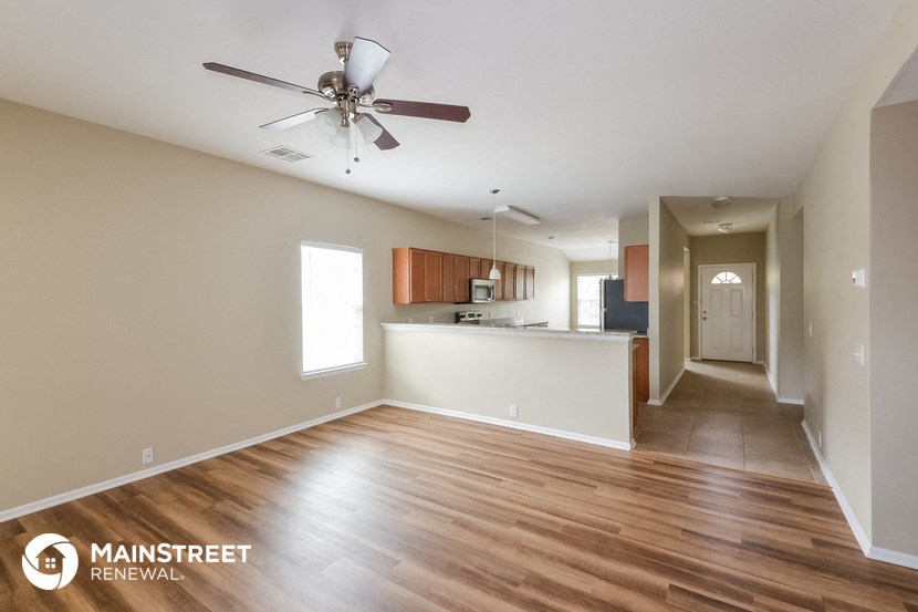 an empty living room and kitchen with wood flooring and a ceiling fan