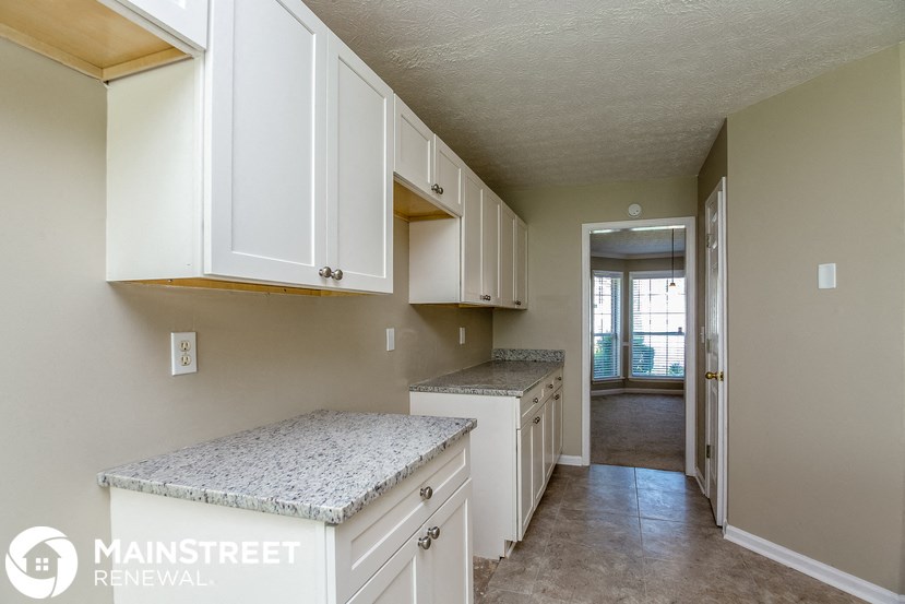 a kitchen with white cabinets and counter tops and a door to a hallway