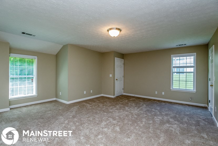 the living room of a house with carpet and two windows