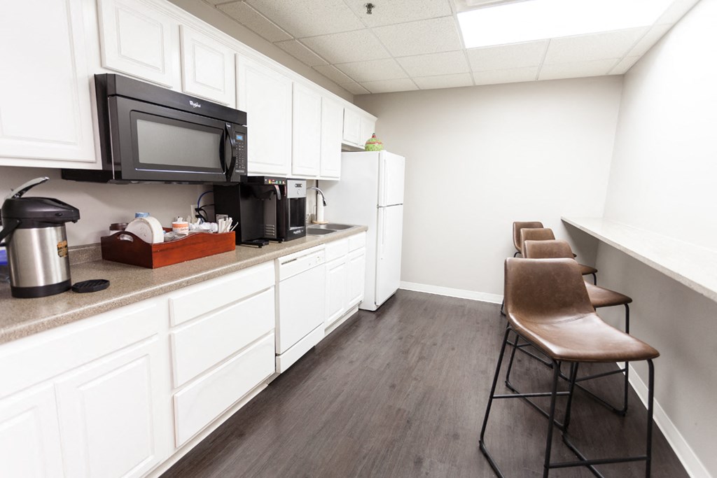a kitchen with white cabinets and a counter with chairs and a microwave