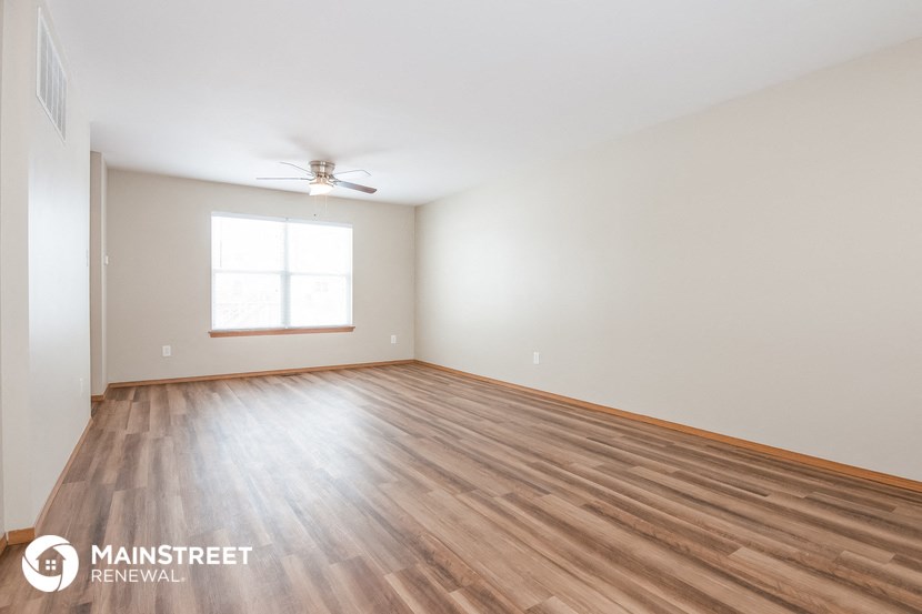 the spacious living room with wood flooring and a ceiling fan
