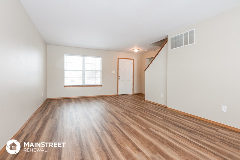 the living room of an apartment with wood flooring and white walls