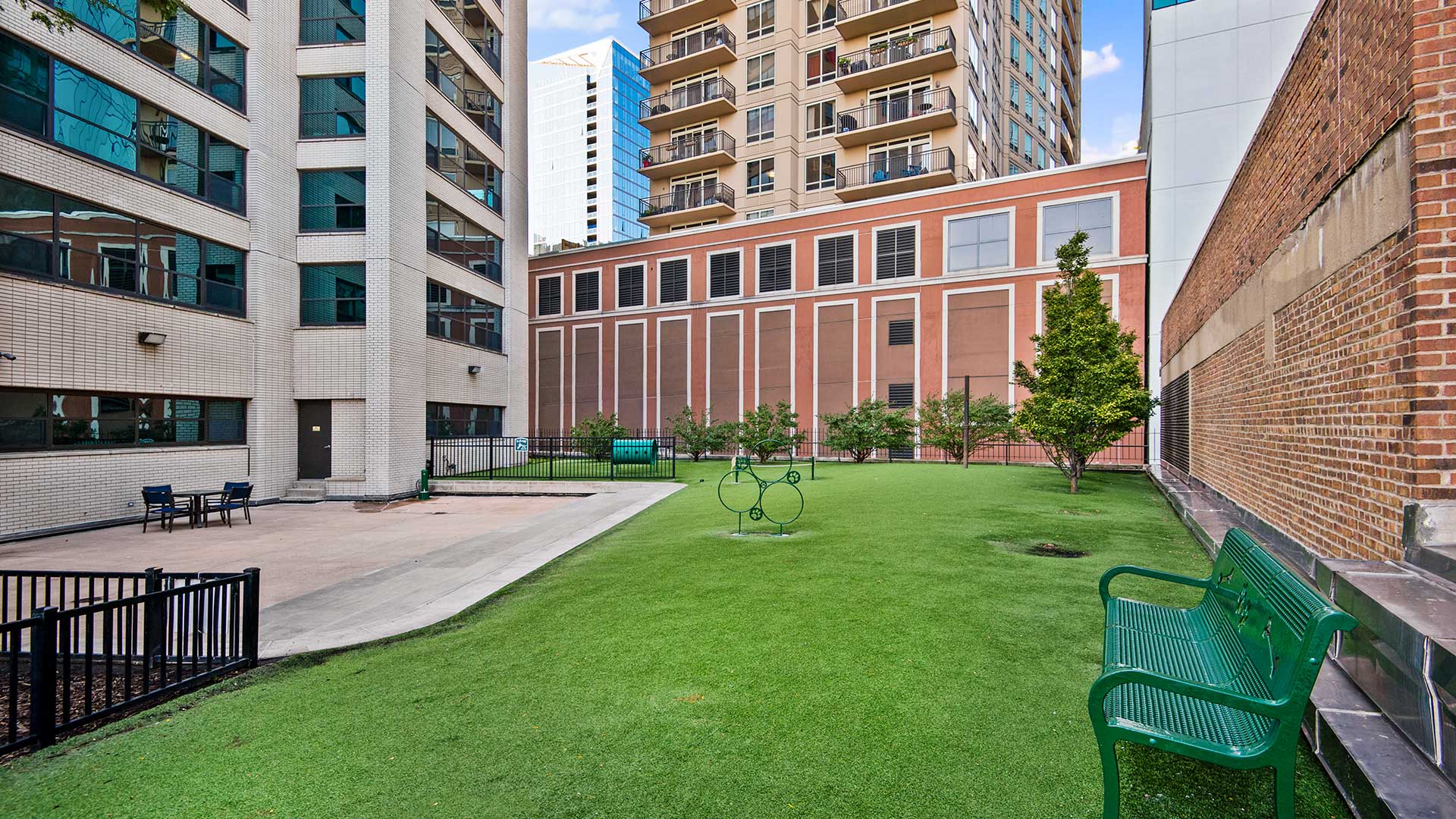 Green turf stretches out across the out door dog park at Eleven Thirty. Buildings rise up around it and various dog exercise equipment pieces are placed around.