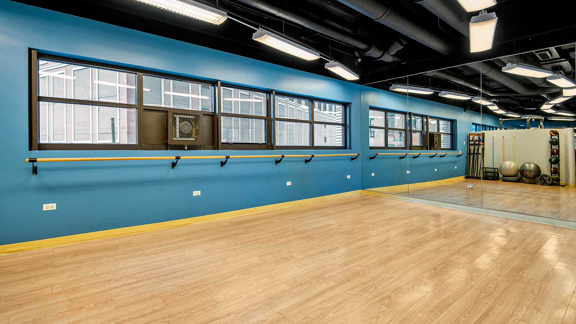 An open fitness studio floor with bar along the far wall and mirrors to the right.