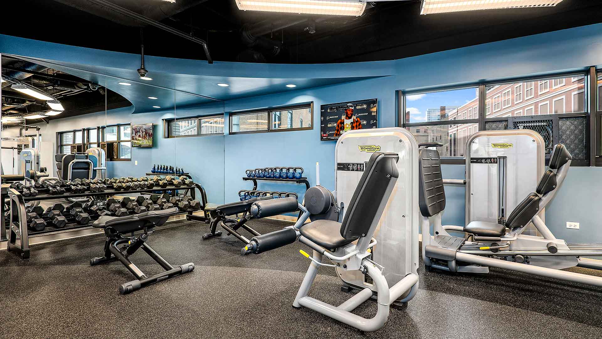 Gym equipment line the right side and free weights are stacked to the left along a mirror wall in the fitness center at Eleven Thirty.