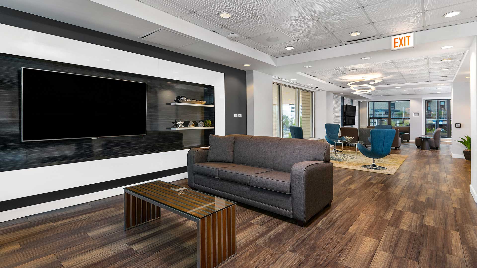 The community room at Eleven Thirty. A couch and coffee table sit beside a large television in the foreground. Additional lunge furniture and another television are the in background.