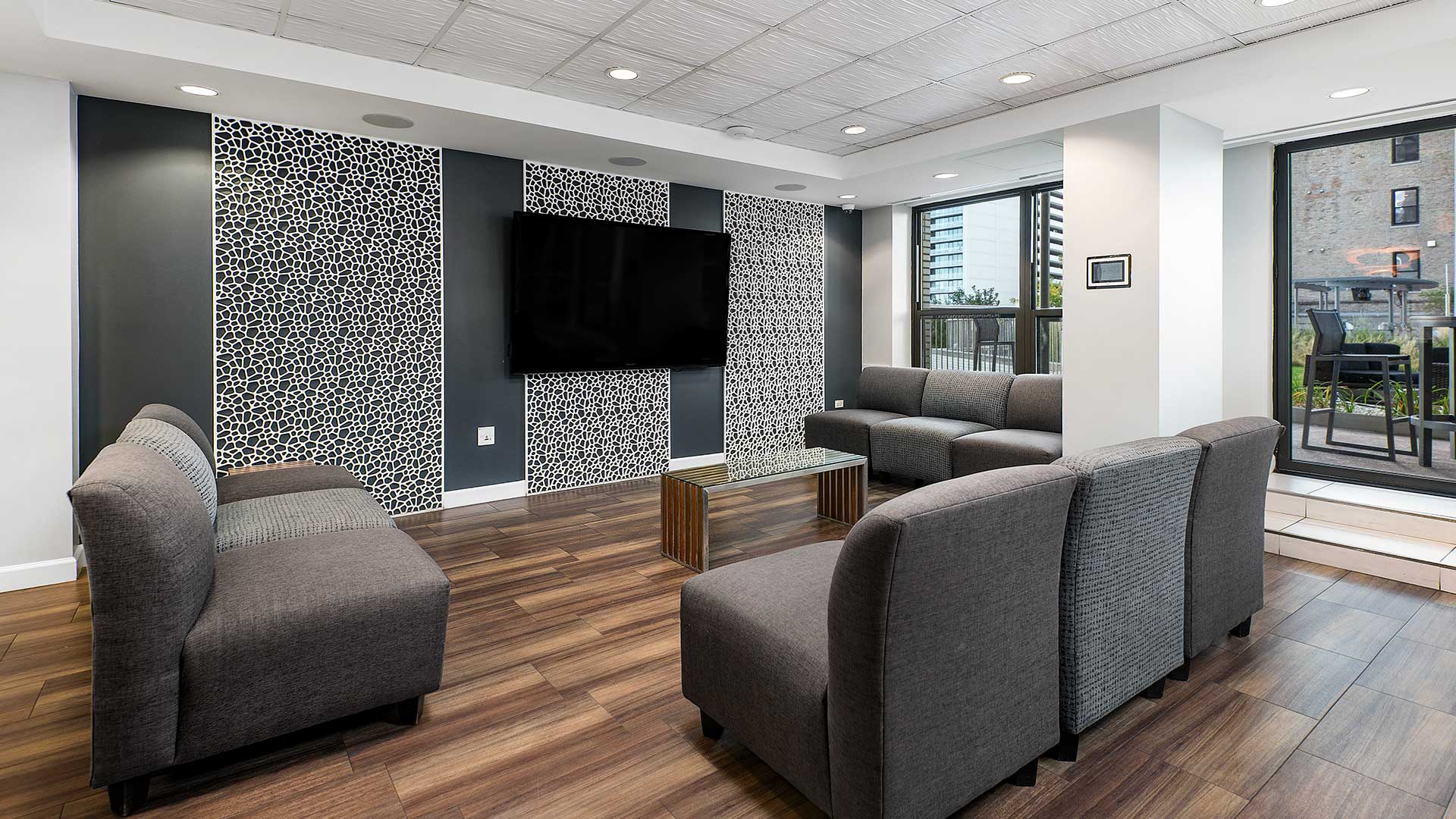 Couches are placed around a coffee table before a large television on the wall. Large windows on the right show the sun and pool deck outside at Eleven Thirty.