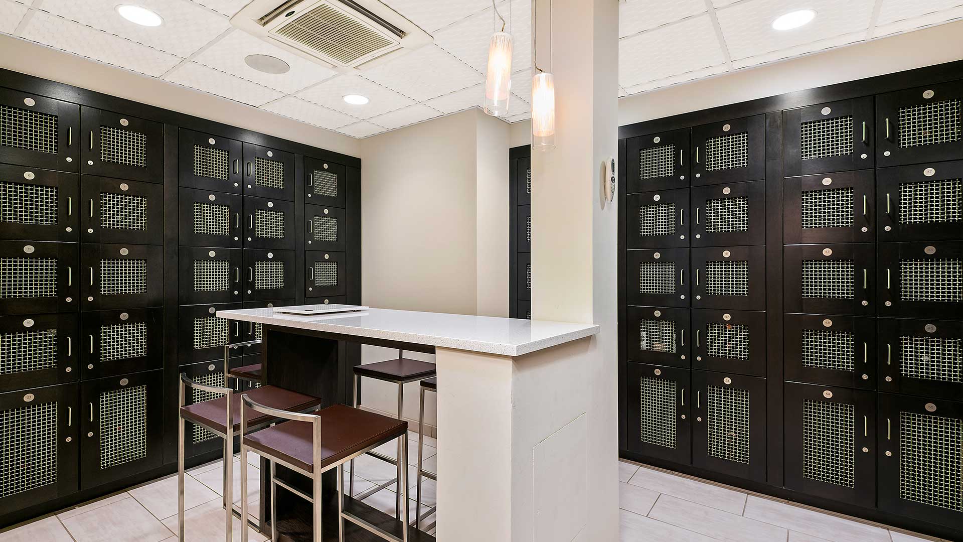 Wine lockers are built into the walls and there is a counter height table in the middle of the room with chairs around it.