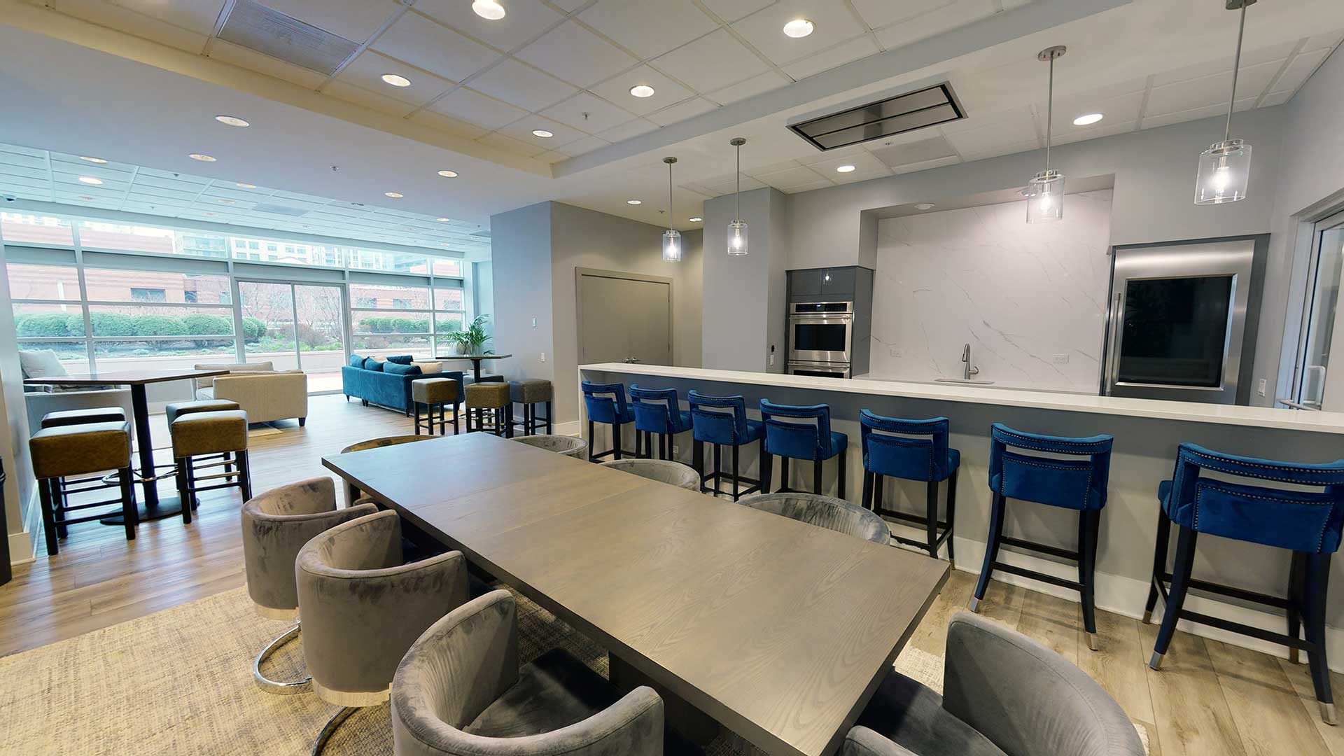 Looking at the bar in the Party Room in Grand Plaza. Stools line the bar. There is a dining table in the foreground. Off to the left is the rest of the Party Room with additional seating.