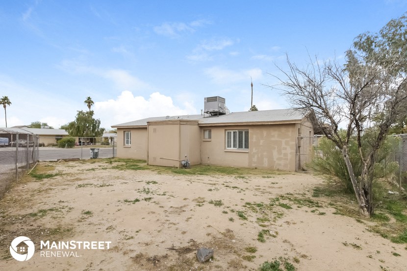 a home in the middle of a dirt lot with a fence and a house