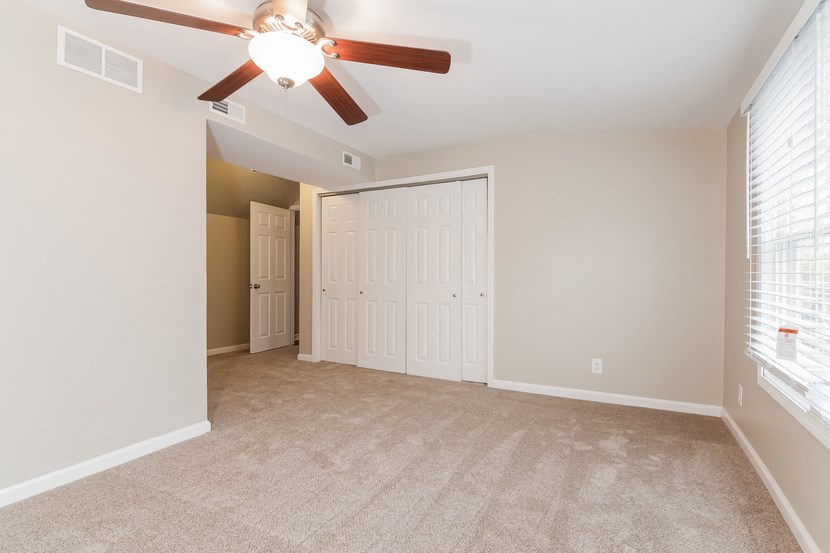 an empty living room with a ceiling fan and a closet
