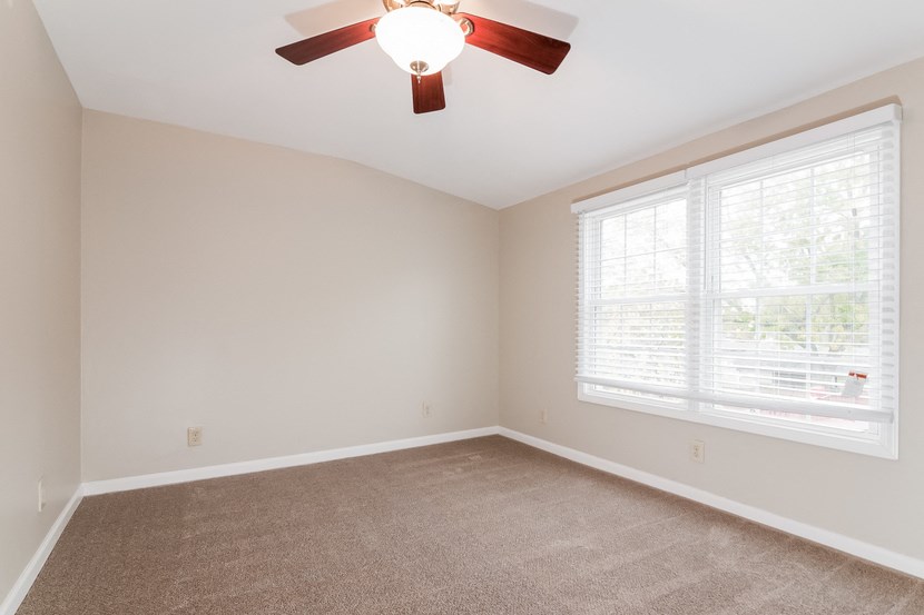 an empty bedroom with a ceiling fan and a window