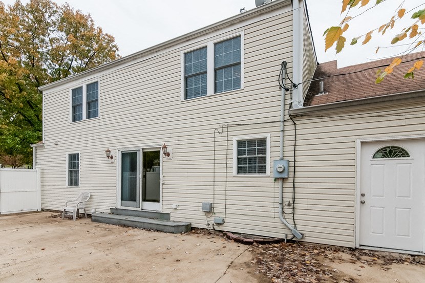 the back of a white house with a driveway and a white door