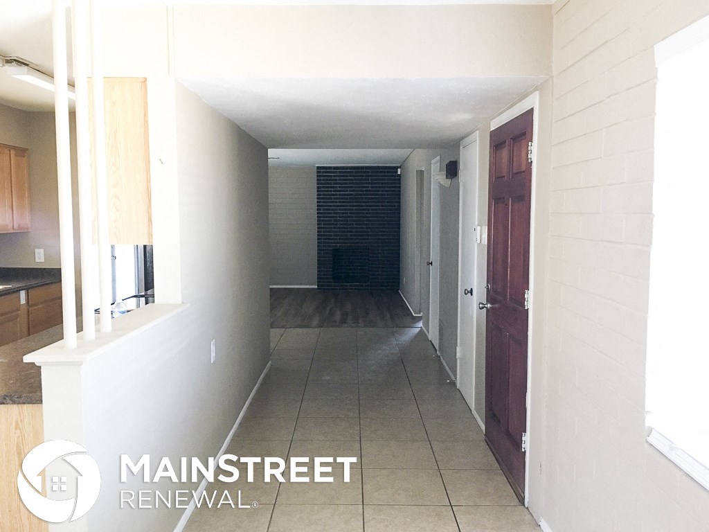 a long hallway with a tile floor and white walls and a wooden door