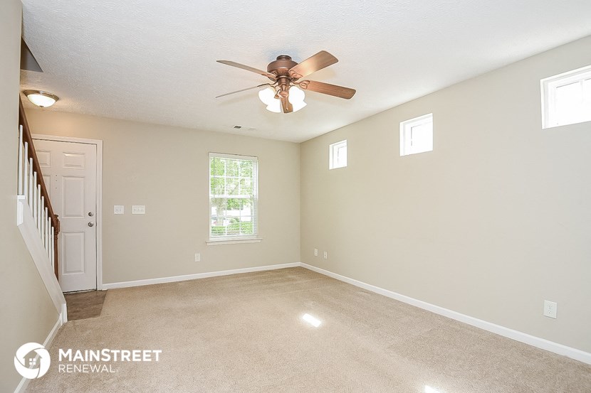 an empty living room with a ceiling fan and a staircase