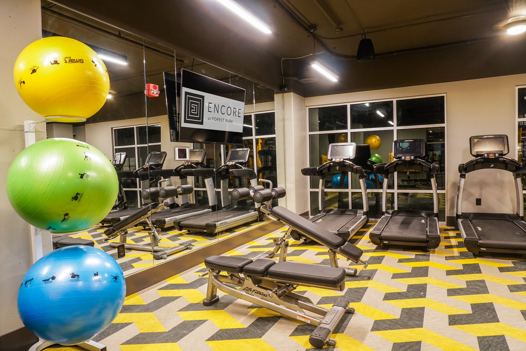 a gym with cardio equipment and exercise balls on the floor
