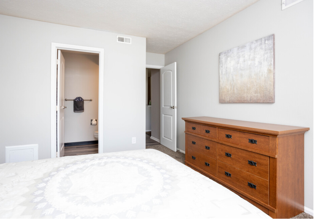 a bedroom with a bed and a dresser and a door to a bathroom