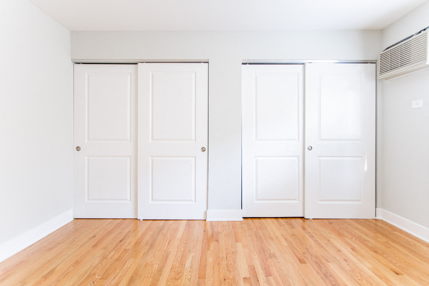 an empty room with white doors and wood floors