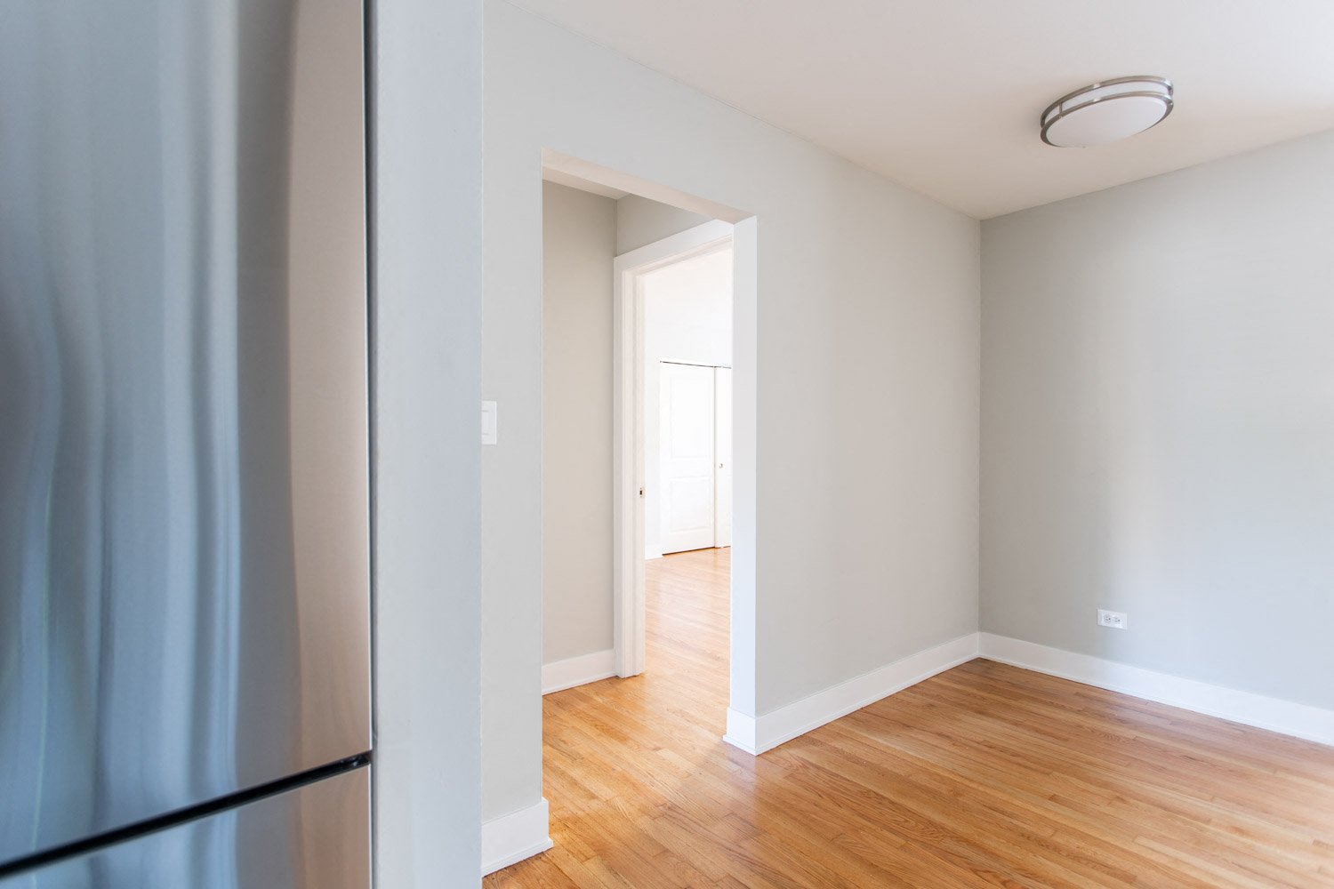 an empty room with a refrigerator and hard wood floors