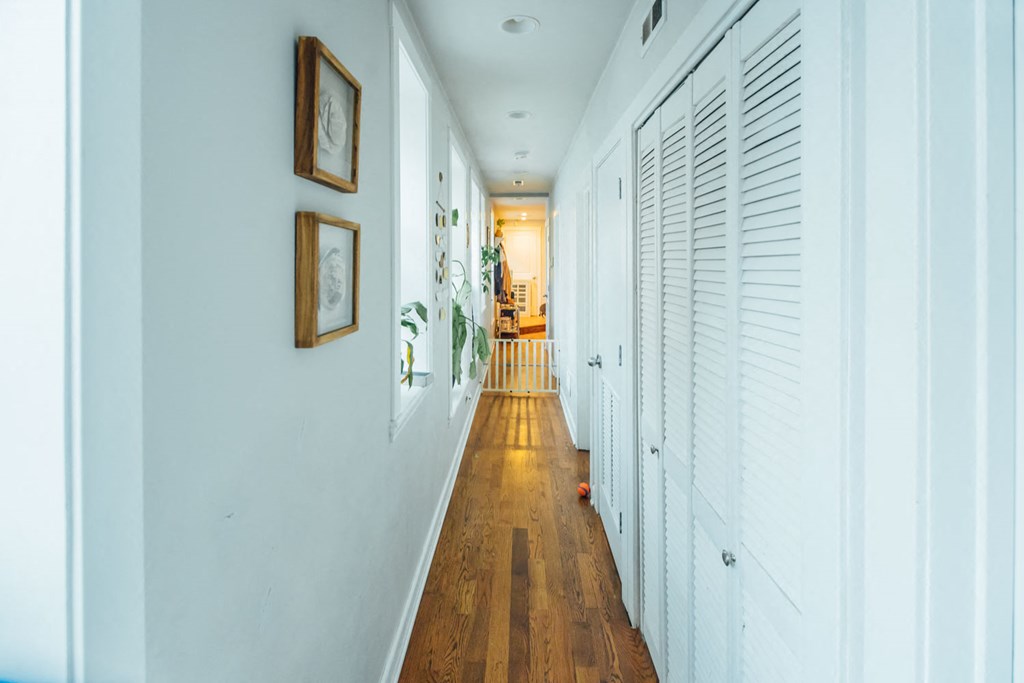 a hallway with white walls and wooden floors and white shutters