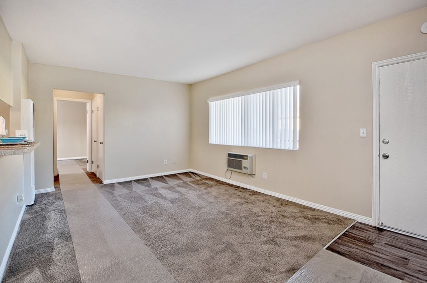 the spacious living room and dining room of an apartment with a large window and carpet