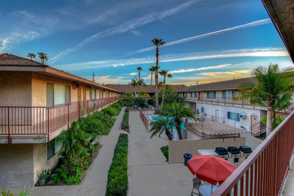 a courtyard with tables and umbrellas and buildings with palm trees
