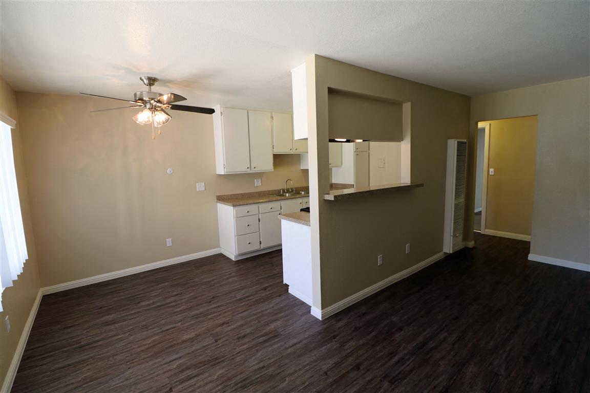 an empty living room with a kitchen and a ceiling fan