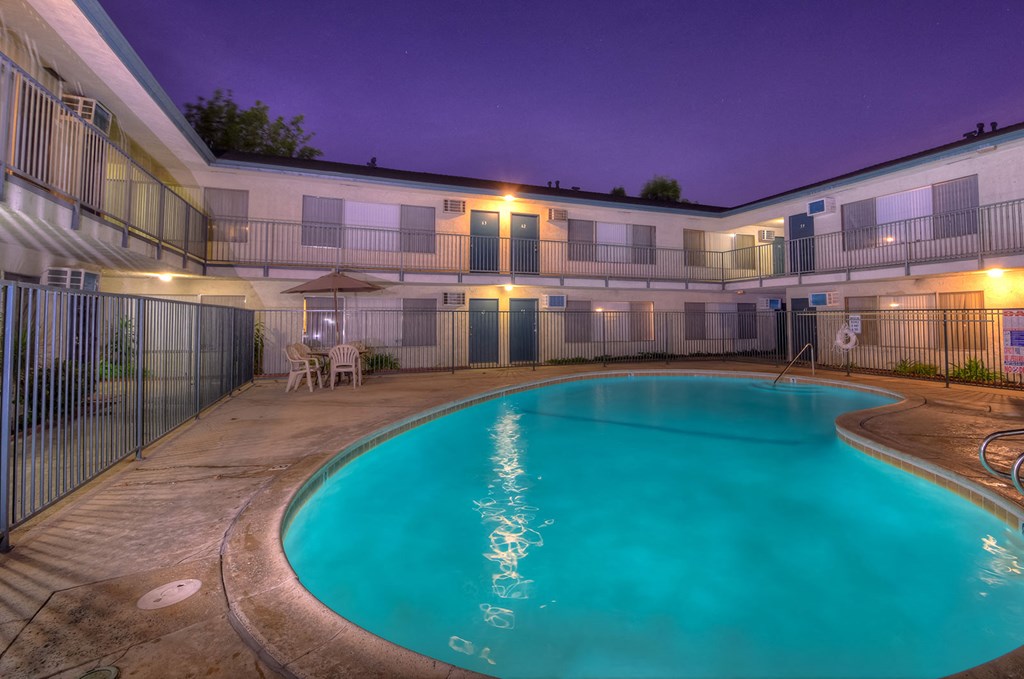 the swimming pool at night at an apartment building with a blue pool