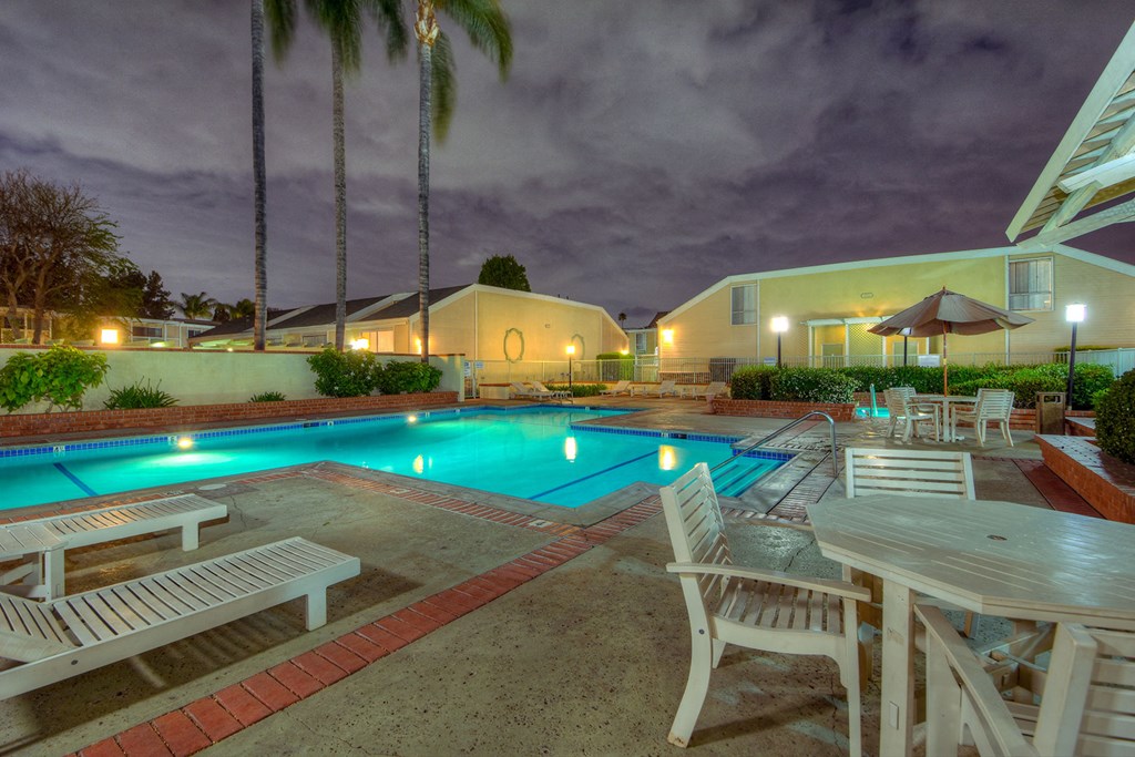 a swimming pool with tables and chairs around it at night