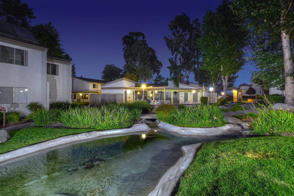a backyard with a pond and a house at night