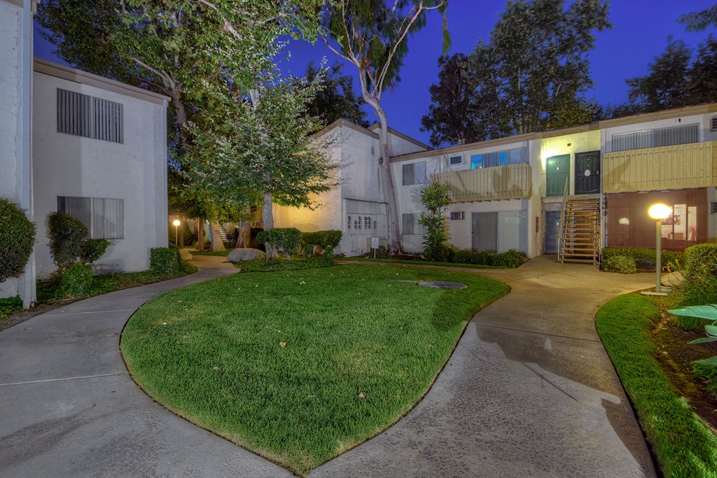 a courtyard between two buildings with green grass and trees