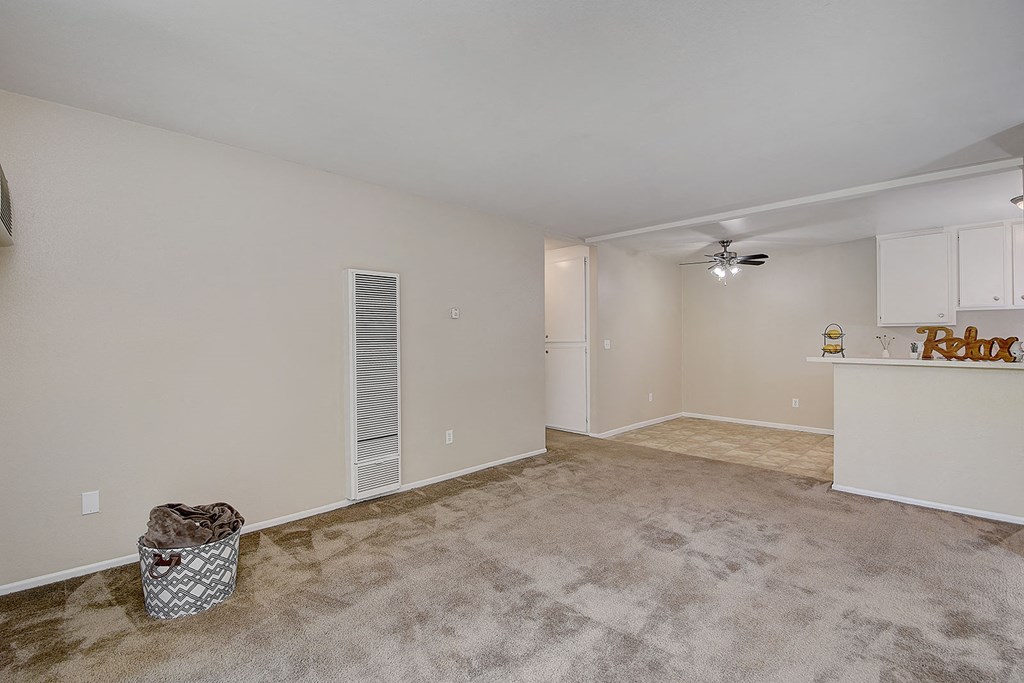 an empty living room with a kitchen and a ceiling fan