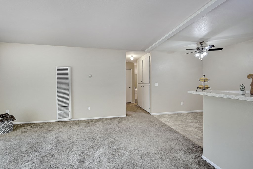 an empty living room with a ceiling fan and a door to a hallway