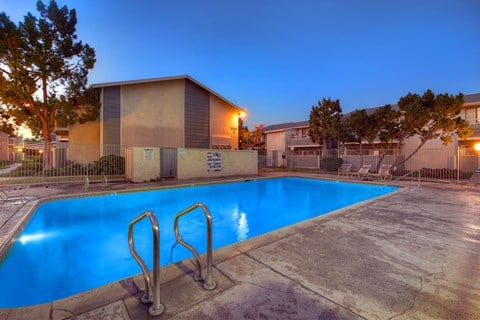 a swimming pool at night at an apartment complex with a blue pool