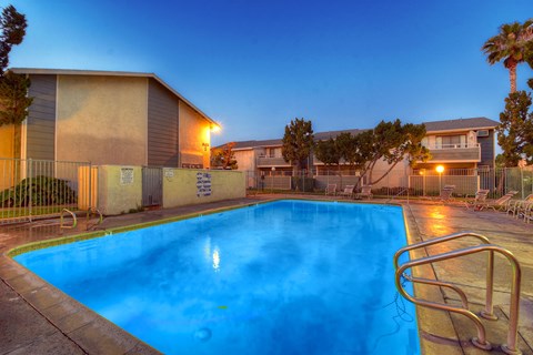a swimming pool at night with apartments in the background