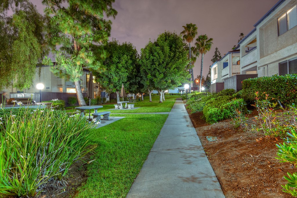 a walkway between two apartment buildings with benches and trees