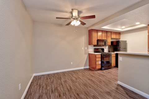 an empty living room with a ceiling fan and a kitchen