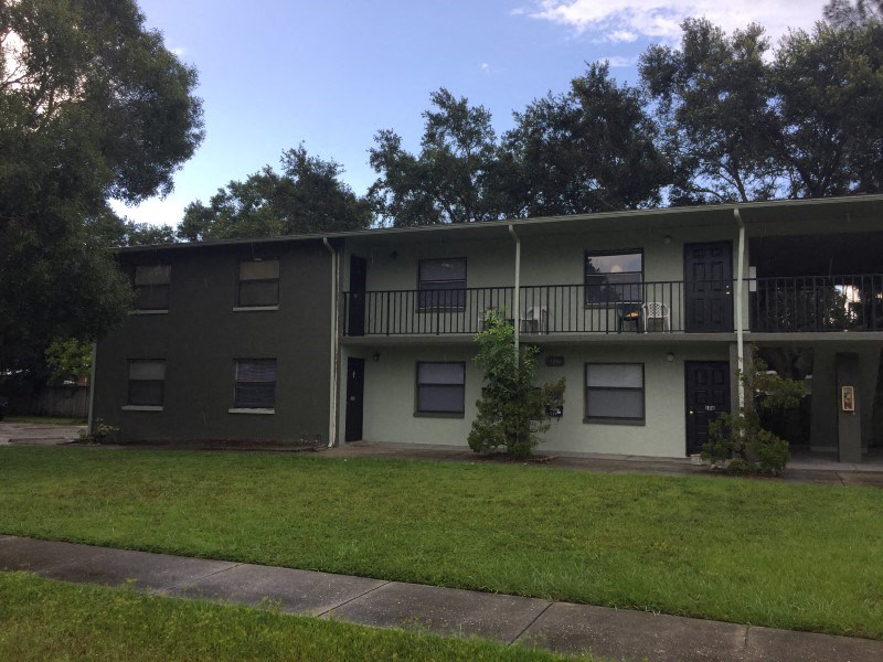an apartment building with a green exterior and a grass yard