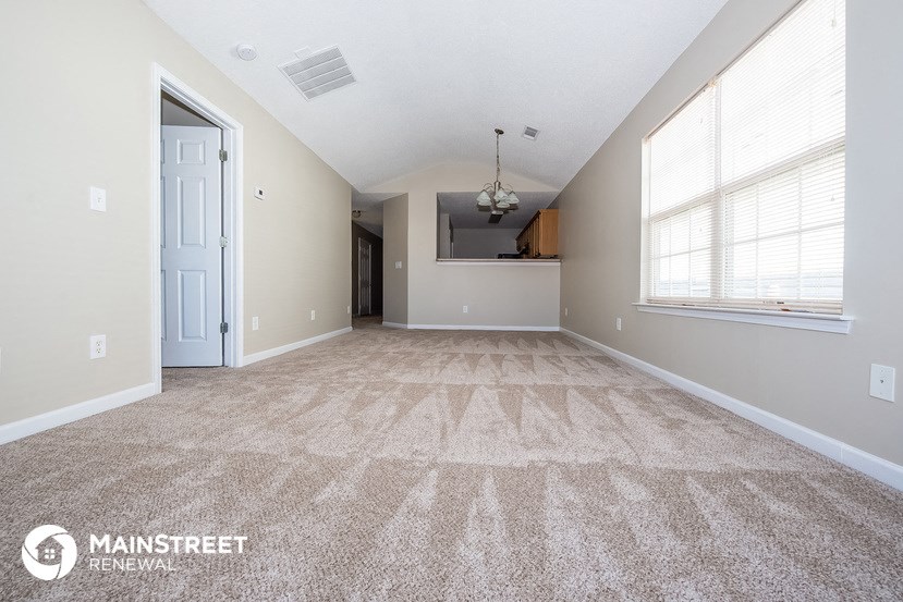 a spacious living room with carpet and a door to the kitchen