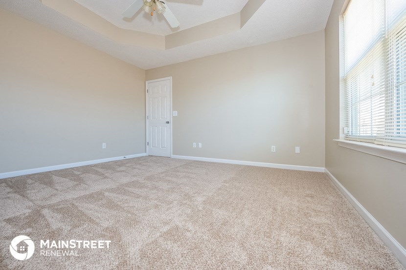 the spacious living room with carpeted flooring and a ceiling fan