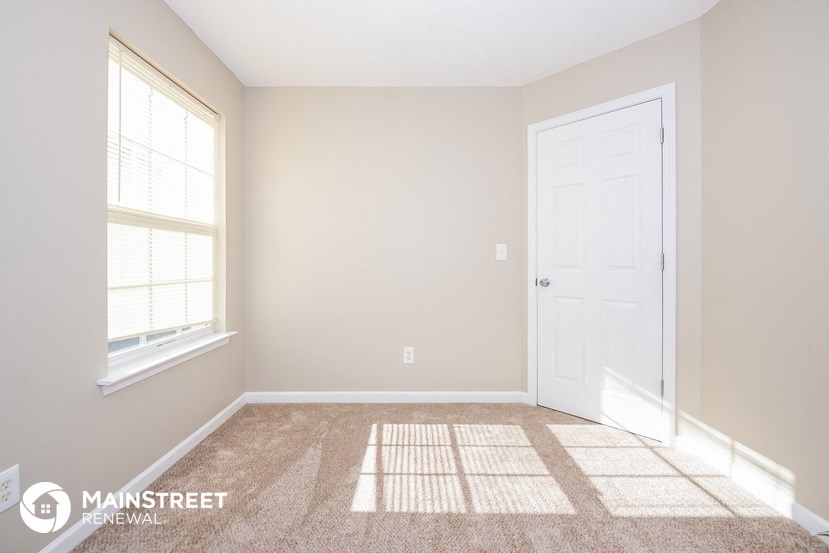 a bedroom with a white door and a window and a carpeted floor