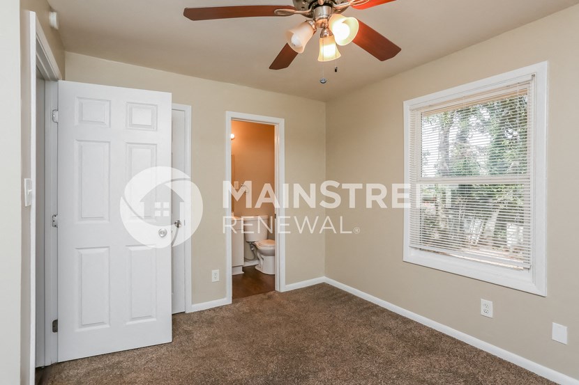 a bedroom with a ceiling fan and a door to a bathroom