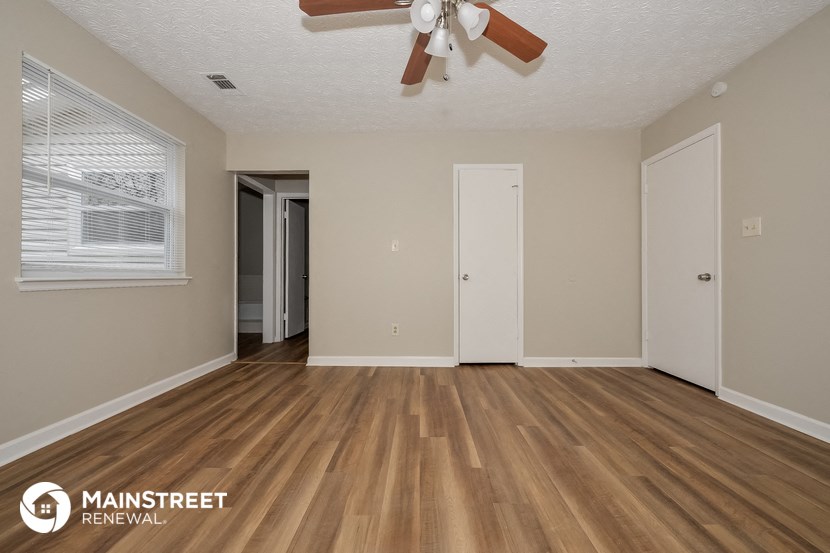 the spacious living room with wood flooring and a ceiling fan